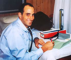 Dr. Thomas Gaziano seated in exam room and taking notes next to smiling female patient
