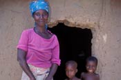 Photo: African woman stands in front of entrance to a hut, children surround her