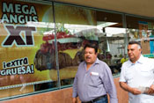 Photo: Large sign picturing fast food hamburger reading Mega Angus XT in window on street, two men walk past