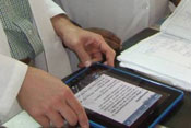 Photo: iPad, held by hands or person wearing white lab coat, placed on desk next to paper file