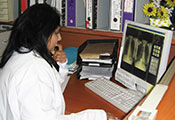 Dr Naidoo in a white lab coat seated at a desk reviews side by side chest x-rays on a computer screen