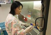 Former Japanese fellow Dr. Junko Murai in lab wearing scrubs, stands next to hood