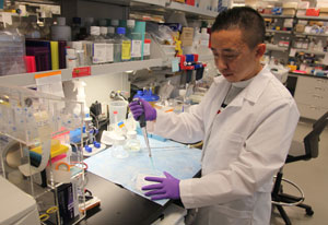 Japanese fellow Dr. Atsushi Tanaka in lab full of materials, wearing white lab coat