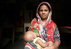 Woman seated indoors breastfeeds a baby.