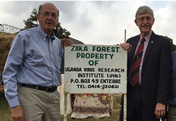 Dr. Francis Collins and Dr. Roger Glass stand in front of the Zika Forest sign in Uganda