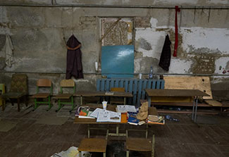 Desks at the former Yahinde school. The tops of he desks are scatted with books, and empty cup, and a teddy bear.