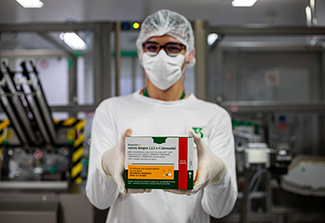 A research worker, wearing a hair net, face mask, and glasses, holding a Butantan Dengue vaccine