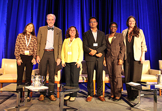 In this photo the panelists from  the “Power, Resources, and Equitable Partnerships” plenary session at CUGH 2024 pose for a photo on a brightly lit stage with a dark blue curtain in the background.