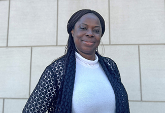 Chinwe Chukwudi wearing a white shirt and black sweater poses in outside of the NIH Clinical Center in Bethesda, Maryland, USA.