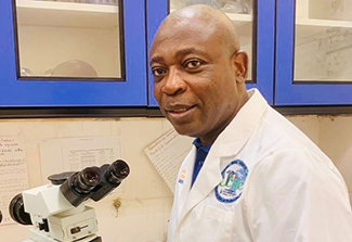 Dr. Seydou Doumbia in a lab coat next to a microscope at the UCRC laboratory