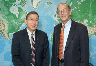 Dr. Roger Glass stands beside Dr. Tikki Pang, WHO's Director of Research Policy in 2007.  Both wear suits and behind them is a map of the world.