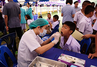 Dr. Waranuch Pitiphat, dressed in a white lab coat, provides dental care to a child. They are pictured seated within a tent wher