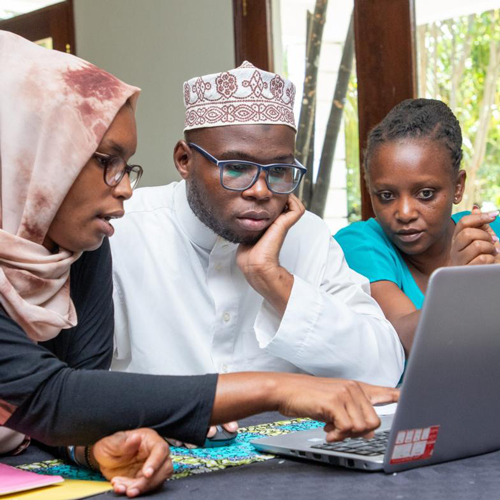 Three African adults sitting at a desk, looking at a laptop.