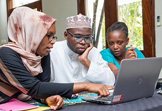 Three African adults sitting at a desk, looking at a laptop.