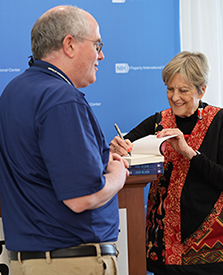 Dr. Jody Olsen, wearing a black sweater incorporating an orange pattern, signs a copy of her memoir for a man seen from behind and wearing a blue shirt.