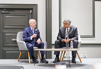 Photo of Dr. Steven Schiff (left) sitting in a chair and speaking into a microphone and Dr. Jay Bhattacharya, sitting in a chair and holding a microphone, listening to Dr. Schiff.