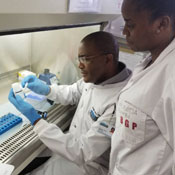 Dr. Moyo Sikhulile and a colleague dressed in lab coats work with sample in the lab