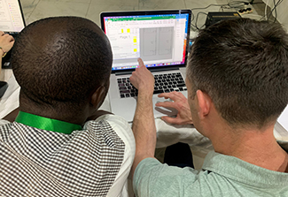 The photo on this page shows trainee Stephan Orafa, UNN-CTAIR, and trainer Neil Dutcher, UCSD, with their backs to the camera as they sit behind a computer screen learning a new skill. 