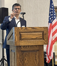 Photo of Dr. Junaid Razzak at a lecture podium with an American flag behind him.