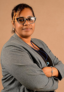 The photo on this page is a headshot of Dr. Sophia Osawe, a member scientist of the BRILLIANT Consortium and former Fogarty fellow. She wears glasses, a gray suit jacket and a black bouse along with a beaded necklace, pearl drop earrings and a silver bracelet. 