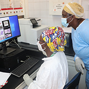 Two researchers in Mali, wearing scrubs and masks, review scientific data on a computer screen