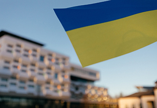 Photo of the Ukrainian Flag waving in the air in front of a building.