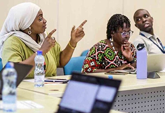 Three African trainees sitting at a desk, the woman on the left speaking.