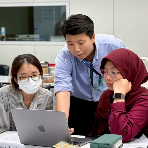 Three colleagues collaborate around a laptop in 