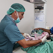 The photo shows Dr. Wilco Zijlmans, wearing surgical scrubs, as he delivers a baby via caesarean section.