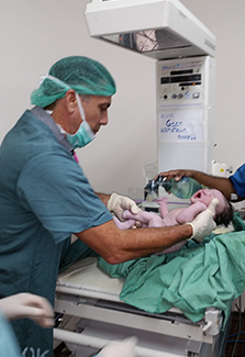 The photo shows Dr. Wilco Zijlmans, wearing surgical scrubs, as he delivers a baby via caesarean section. 
