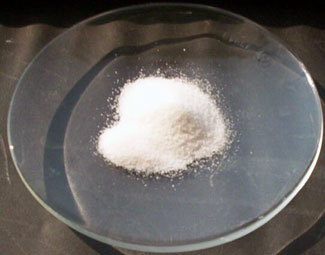 Close-up of arsenic trioxide, a mound of white powder in the middle of a glass dish