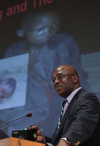 Dr. Tshala-Katumbay stands at podium, slide displayed in background