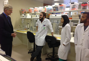 Dr Francis Collins stands in lab across from three young Brazilian researchers in white lab coats