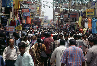 City street very crowded with pedestrians, tall buildings with signs and merchandise line the street