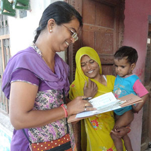 Woman researcher taking notes while speaking interacting with woman holding young child, more children look on