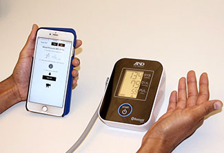Close up of hands using blood pressure monitor next to a smartphone