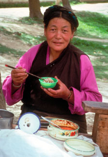 Asian woman eats using chopsticks seated at an outdoor table