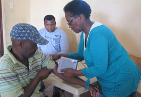 Man seated, arm on table, woman clinic worker places arm cuff around bicep to take blood pressure