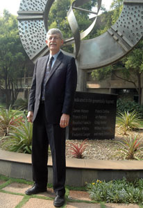NIH Director Dr Francis S Collins stands in front of large genomics-inspired status in India