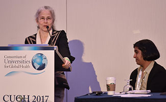 Female speaker speaks at a podium with sign that reads CUGH 2017, seated panel member looks on