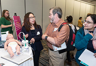 CUGH meeting attendees explore research displays and demonstrations in a conference room