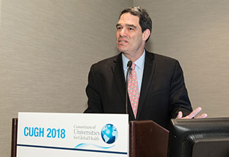 Dr. Jeffrey Blander speaks from a podium labeled CUGH 2018 in a conference room