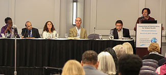 During the CUGH 2019 annual meeting woman speaks at podium next a table of five panelists.