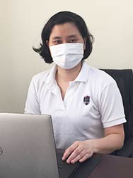 Dr. Dang Hoang Minh wearing a mask working on a computer at a desk in an office.