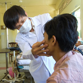 male doctor wearing mask examines patient seated in hospital bed, facing away from camera