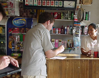 Man collects data from woman behind counter of a shop, researcher working on tablet in foreground