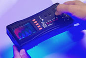 Close up of hands holding FDA Counterfeit Detection Device-3 CD-3, black electronic box with many buttons emits glow on bottom