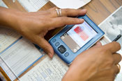 Close up of hands holding PDA displaying data, on top of papers and desk