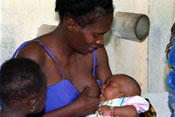 Woman breastfeeding a young baby, a young child seated next to the mother looks on