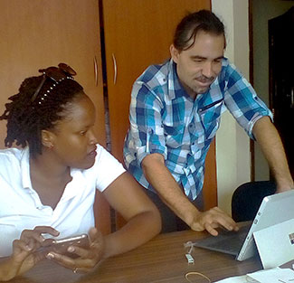 In office, Dr. Eric Coker standing works on a tablet while woman working with a smartphone looks on.